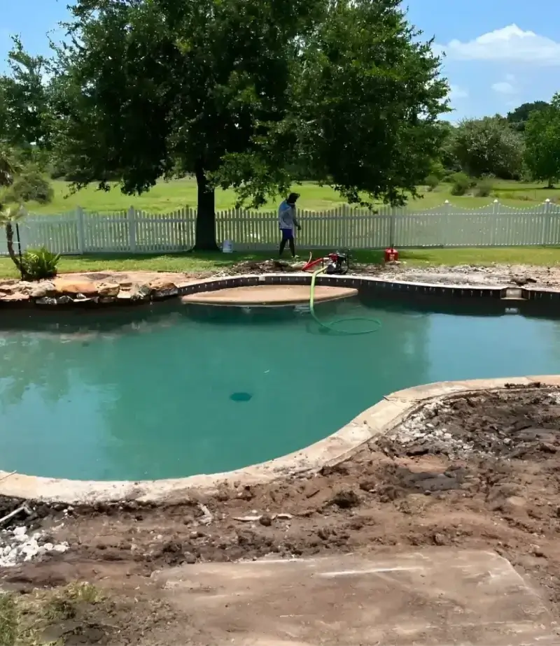 Partially drained swimming pool under renovation with landscaper nearby.