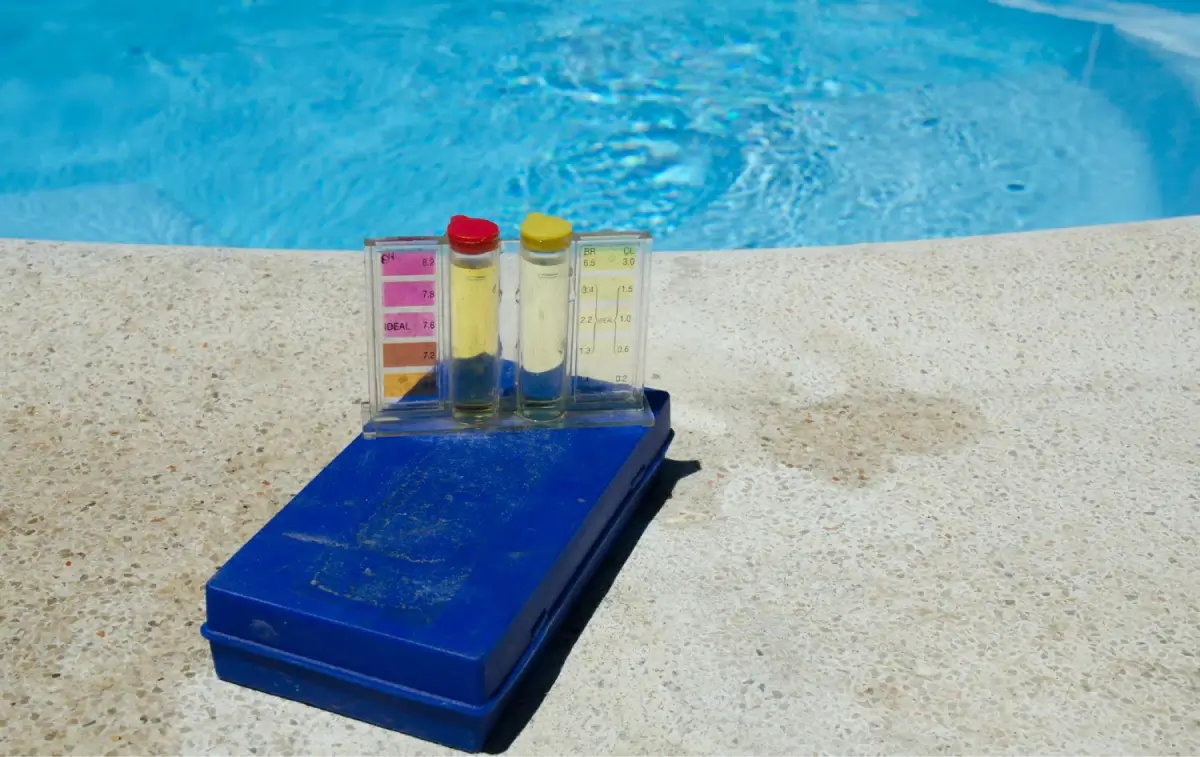 Pool water testing kit with color-coded vials and scale, placed on the poolside.