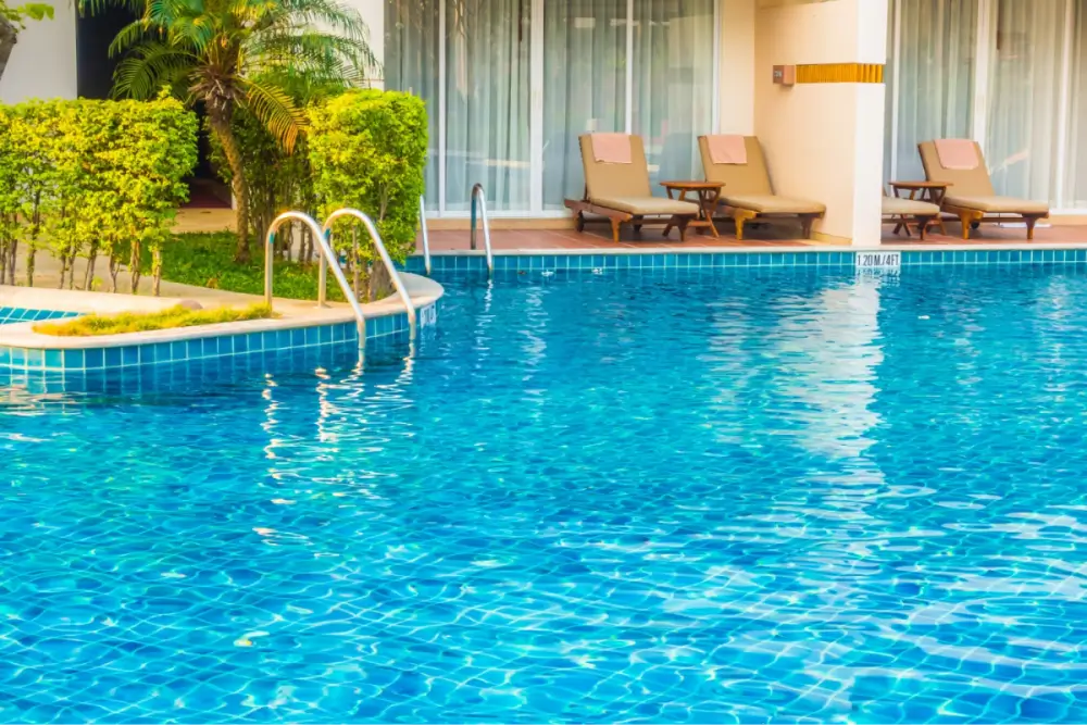 Outdoor swimming pool with a ladder and lounge chairs surrounded by greenery.