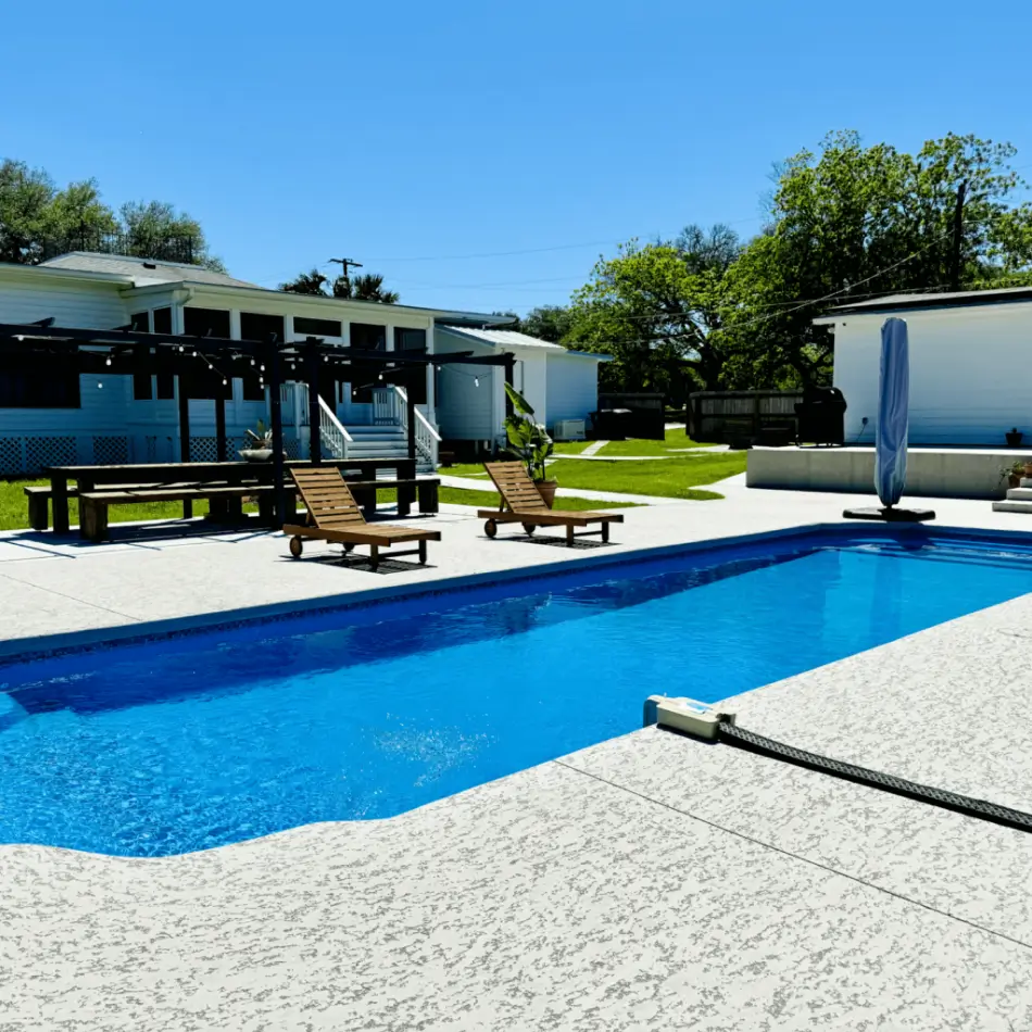 Outdoor pool with lounge chairs and pergola in a sunny backyard.