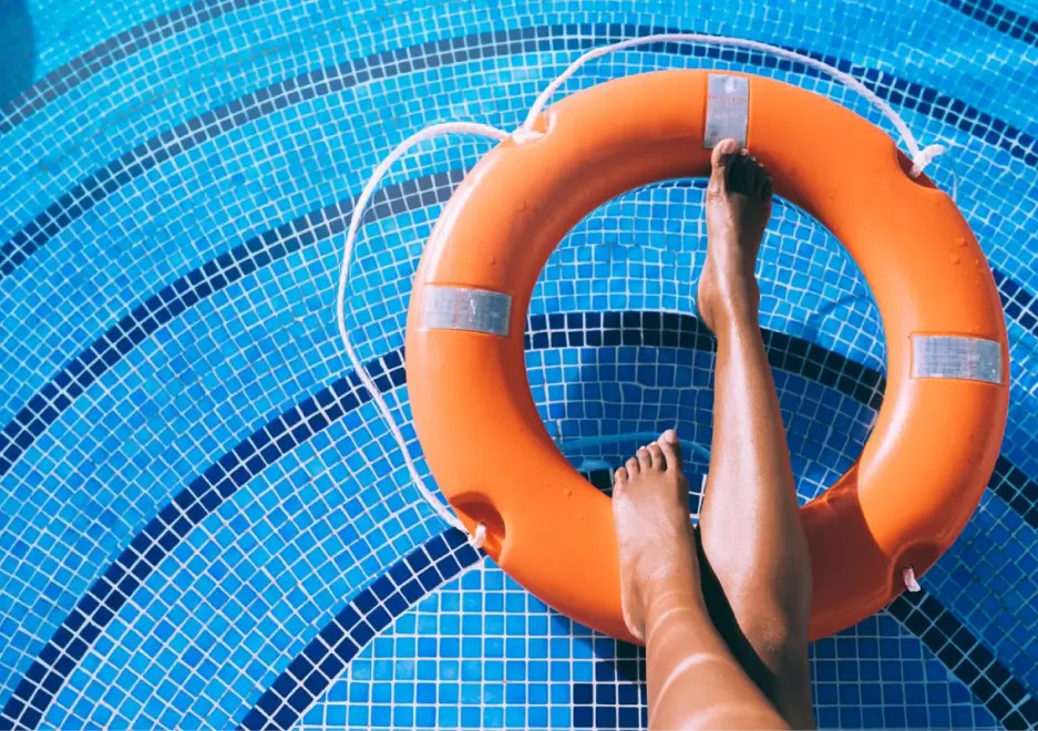 Person relaxing in a pool with legs on an orange life buoy.