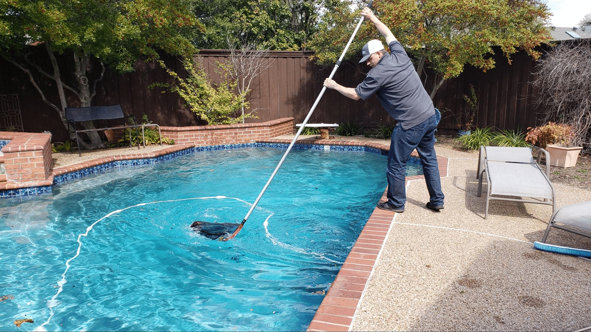 A person using a long-handled net to clean a pool manually.