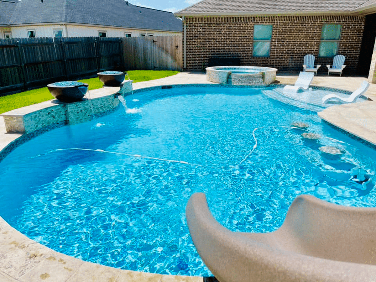 A backyard pool featuring fountains, a hot tub, and lounge chairs on a sunny day.