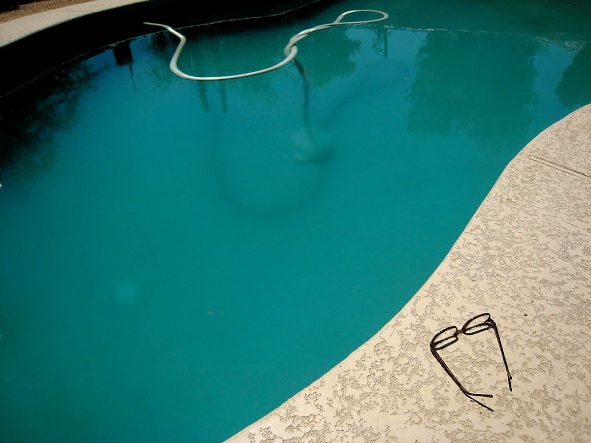 A clear swimming pool with cleaning equipment and a pair of glasses placed on the edge.