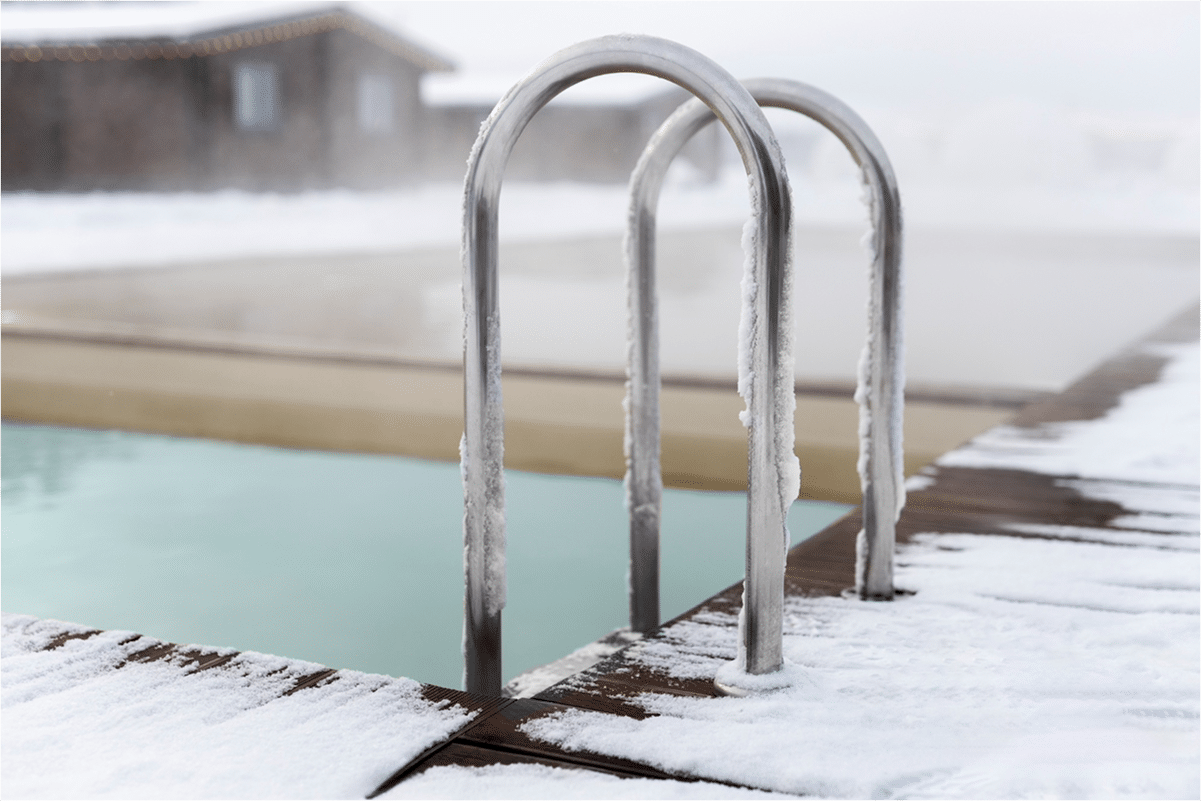 A close-up of a pool ladder covered in frost, surrounded by snow on the pool deck.